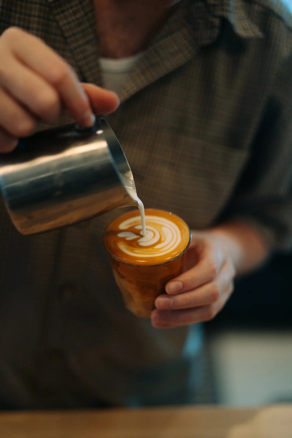 A barista pouring latte art into a glass cup